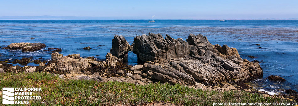a unique rock structure with striated formations creating an arch at the shoreline